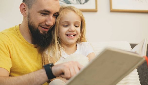 Vidám szőke lány és szakállas apja együtt olvasnak egy könyvet. - Fotó, kép