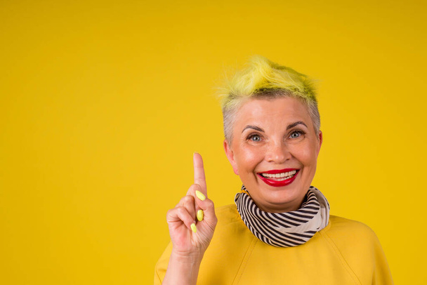 mature woman with colored stylish yellow dyed hair and red lipstic lips in warm dress background studio copy spase.forever young soul - Φωτογραφία, εικόνα