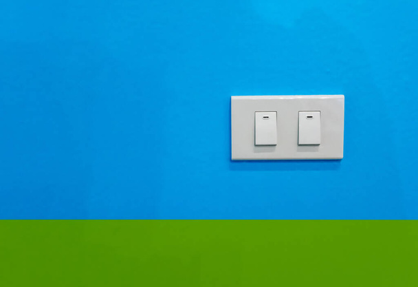 Белый двойной электрический выключатель на синем и зеленом фоне
. - Фото, изображение