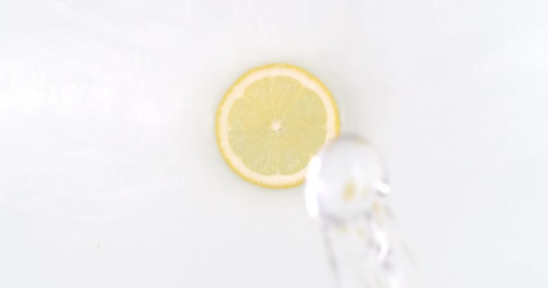 Sobre un fondo blanco, un chorrito de agua cae sobre una rodaja de limón en cámara lenta
 - Metraje, vídeo