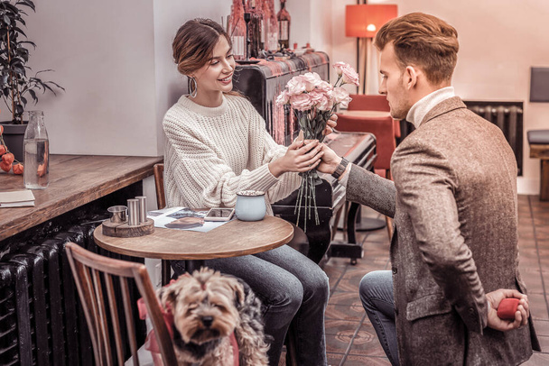 Scene in cafe. Man standing on the knee gifting flowers to girlfriend about to propose - Foto, Imagem