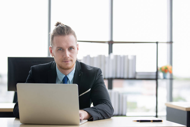 Portrétní snímek pohledného bělošského podnikatele, který aktivně používá notebook v moderní kanceláři. - Fotografie, Obrázek