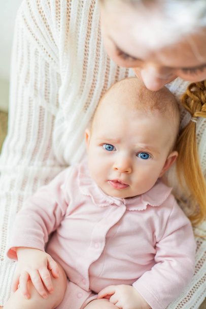 Kaunis nuori äiti pitää sylissään pientä sinisilmäistä kaksikuukautista tytärtä. Vastasyntynyt. Kulta.
. - Valokuva, kuva
