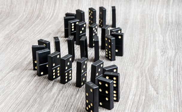schwarze Dominosteine auf einem hellen Holztisch stehen in einer Reihe, selektiver Fokus, Black old, vintage Dominosteine auf einem Papphintergrund. Das Konzept der Dominosteine - Foto, Bild