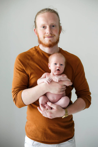 Closeup portrait of young bearded Caucasian father hugging and kissing newborn baby.Male man parent holding child.Authentic lifestyle touching tender moment.Single dad family life concept.Studio portrait of a happy father with a baby in his arms - 写真・画像