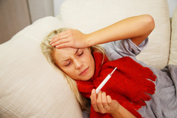 Jeune femme malade avec thermomètre couché sur le canapé à la maison
 - Photo, image