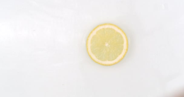 On a white background, a splash of water falls on a slice of lemon in slow motion - Video, Çekim