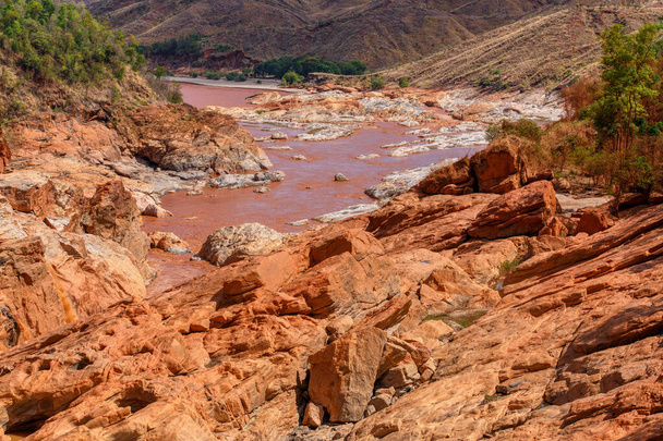 Rotsachtige rivierbedding Betsiboka rivier na zware regenval, rood gele waterstroom, noordelijk Madagaskar landschap - Foto, afbeelding