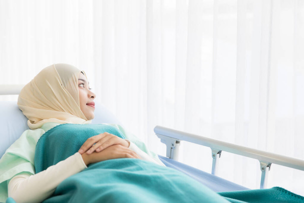 Молодая и красивая мусульманка в хиджабском платье лежала одна на кровати в больнице. Она смотрит далеко на улицу, как будто ждет, что кто-то навестит ее. Идея для ощущения одиночества и страха пациента
. - Фото, изображение