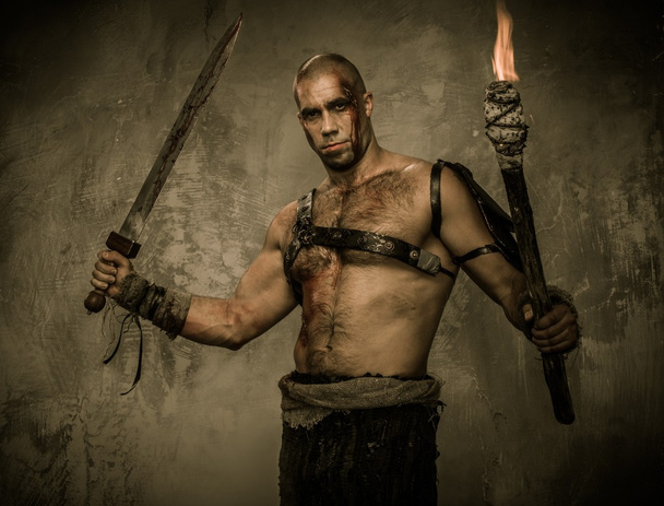 Wounded gladiator holding torch and sword covered in blood - Photo, Image