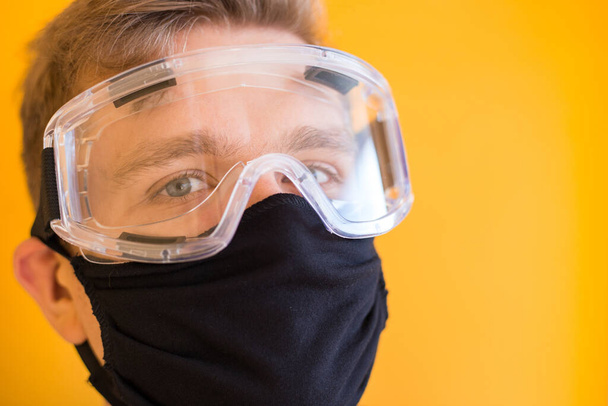 Man in protective glasses, medical mask on yellow background. Way to protect against coronavirus. Covid-2019, Pandemic 2020 - Photo, Image