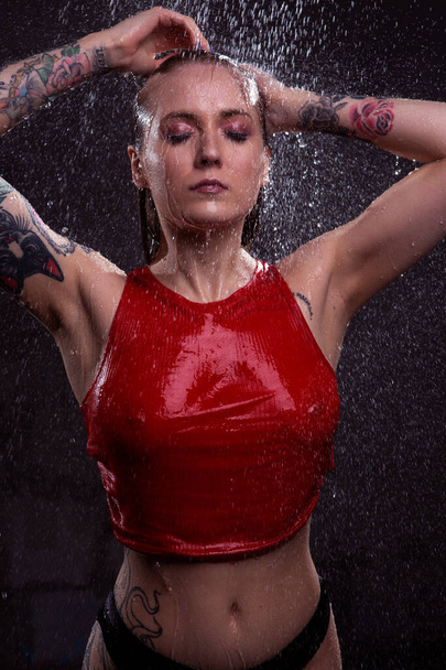 Portrait of a sexy girl with a beautiful body and neat Breasts standing in bright splashes of water in wet underwear. Studio portrait of aquastudio - Фото, зображення