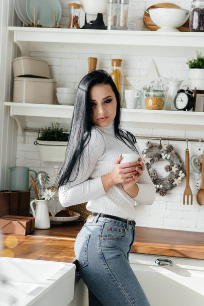 Beautiful young girl has breakfast and drinks coffee in the kitchen. Lifestyle. - Photo, image
