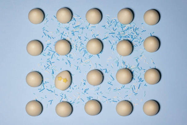 A pattern of chocolate eggs with one egg with star-eyes tilted slideways on a blue background - Photo, Image