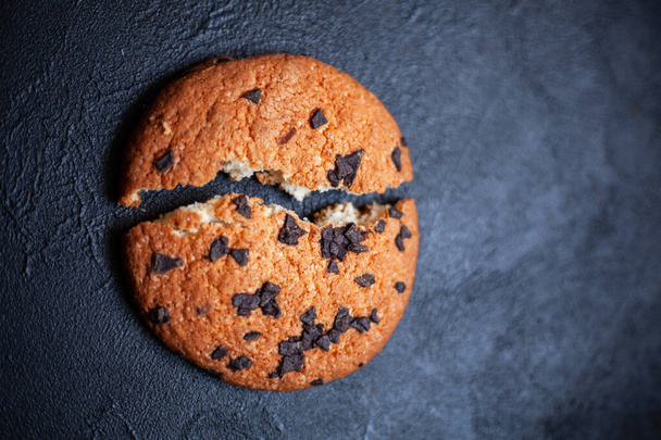 One broken cookie in two pieces, with chocolate on a black background. Image for an inscription. - Фото, изображение