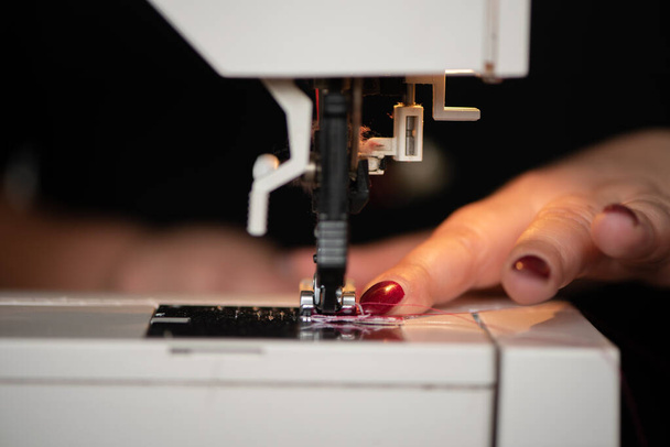 détail des femmes mains couture maching couture couture vêtements en tissu rouge sur une machine à coudre. Œuvre à la lumière de la lampe matérielle intégrée. Aiguille en acier avec boucle et pied presseur close-up
 - Photo, image