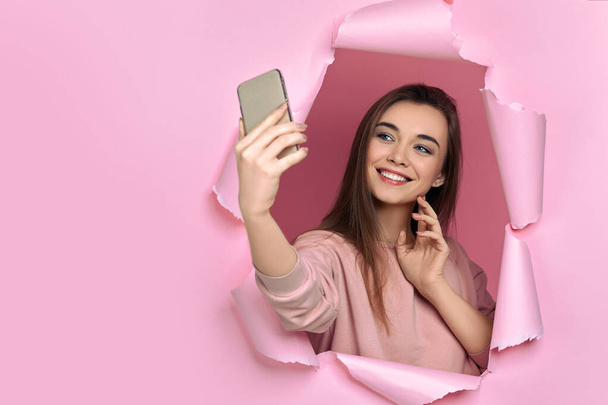 girl holding smart phone in hand in torn paper pink wall - Foto, Imagen