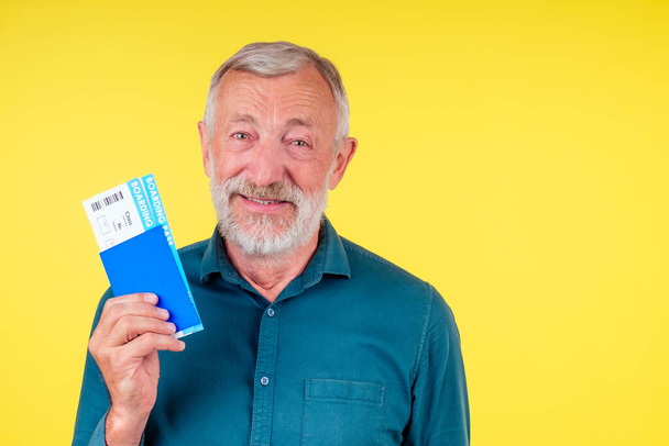 smiling senior man holding passport in blue cover and tickets studio yellow background - Foto, afbeelding