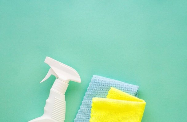 Cleansing spray with colored rags on a mint background - Foto, afbeelding