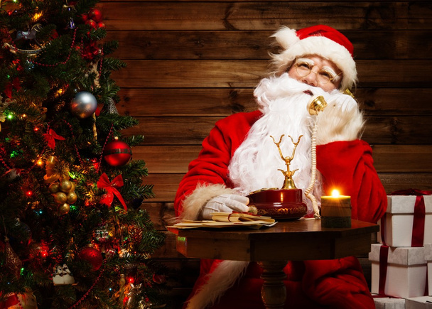 Санта-Клаус разговаривает по телефону в деревянном интерьере дома
 - Фото, изображение