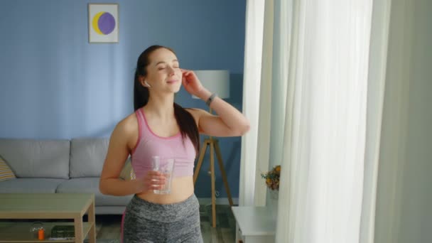 Frau steht im Wohnzimmer und trinkt Wasser - Filmmaterial, Video