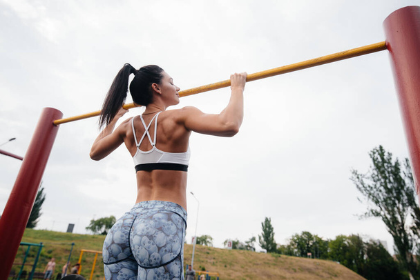 Sexy girl is pulled up on a horizontal bar in the open air. Fitness. Healthy lifestyle - Zdjęcie, obraz