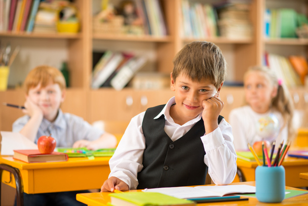 okulda ders sırasında okul masanın arkasında oturan küçük bir okul çocuğu - Fotoğraf, Görsel