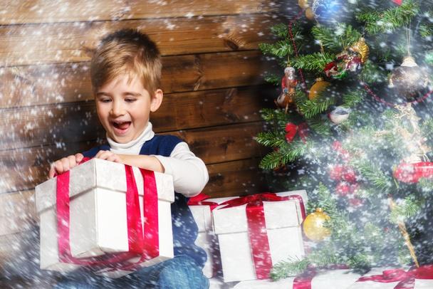 LIitle boy opening gift box under christmas tree in wooden house interior - Photo, Image
