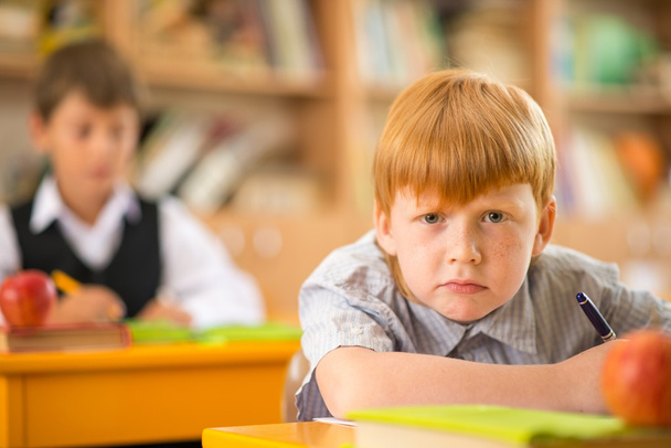 Küçük kızıl saçlı liseli okul ders sırasında masanın arkasında - Fotoğraf, Görsel