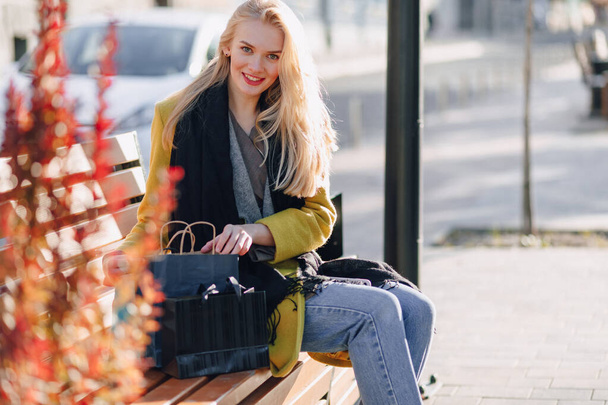 linda mujer rubia atractiva feliz con paquetes en la calle en clima cálido y soleado. compras y emociones positivas
. - Foto, Imagen