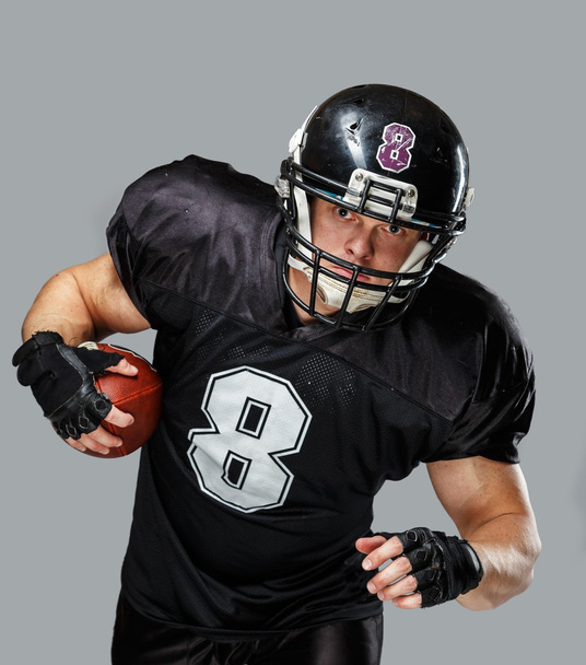 αμερικανικό ποδόσφαιρο παίκτης με μπάλα φορώντας κράνος και Τζέρσεϋ - Φωτογραφία, εικόνα
