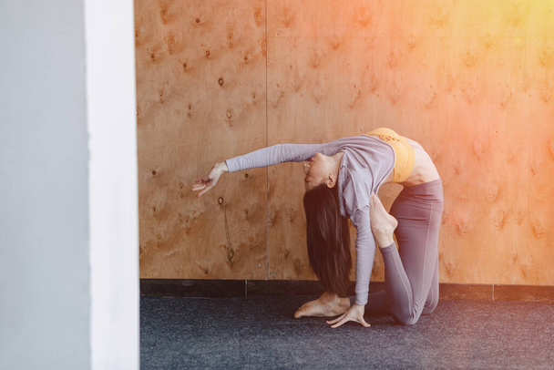 Acogedora joven atractiva haciendo ejercicios de fitness con yoga en el suelo sobre un fondo de madera en el gimnasio
 - Foto, Imagen