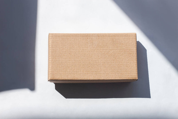 Kraft cardboard post parcel with natural sunlight shadow on white background in creative minimalism style.Brown eco gift box, online shopping concept.Shop super sales,discount tag special offer banner - Fotoğraf, Görsel