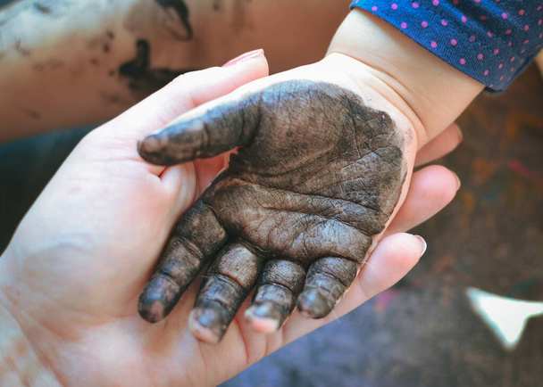El niño se ensució las manos con esmalte de uñas negro. Las palmas de un niño en pintura negra. Manos de niño. Bebé dibuja con las manos
 - Foto, Imagen