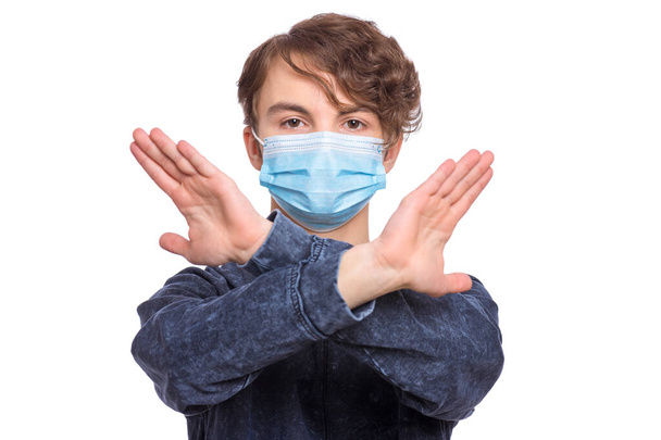 Concept of coronavirus quarantine. Child wearing medical protective mask during flu virus, making stop gesture. COVID-19. Student teen Boy doing stop sign with crossed hands, isolated on white. - Photo, Image