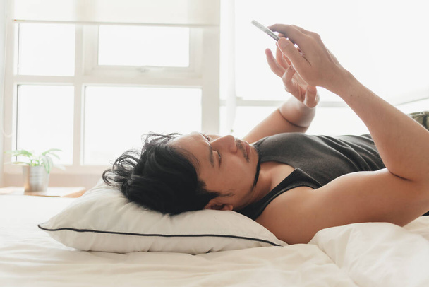 Somnolent homme utilise smartphone tout en étant couché sur le lit. - Photo, image