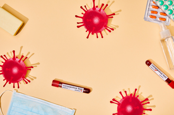 top view of drawn virus near test tubes, soap bar, medical mask, pills and hand sanitizer on beige  - Fotó, kép