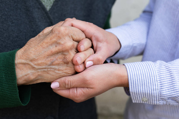 Κοντινή φωτογραφία του φροντιστή που κρατάει τα ζαρωμένα χέρια μιας ηλικιωμένης γυναίκας  - Φωτογραφία, εικόνα