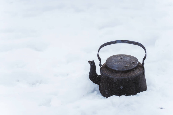Black camp kettle in the snow. Black teapot on a white background. A blackened teapot on a winter picnic - Photo, Image