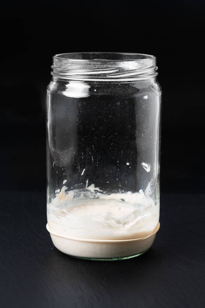 Élelmiszer-koncepció Házi készítésű Sourdough Kezdő vagy kovászos élesztő erjesztett keveréke liszt és víz üvegedényben fekete palakőtáblán - Fotó, kép