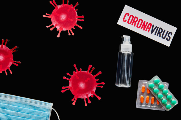 top view of paper with coronavirus lettering near medical mask, pills and hand sanitizer isolated on black  - Fotoğraf, Görsel