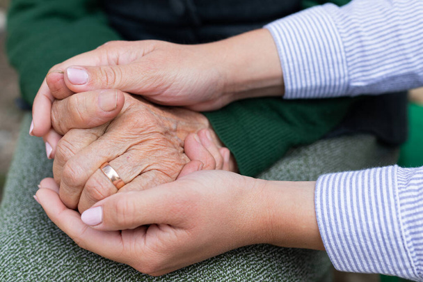 Imagem de perto do cuidador segurando as mãos enrugadas da mulher idosa
  - Foto, Imagem