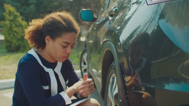 Upset black woman checking car scratches outdoors - Materiał filmowy, wideo