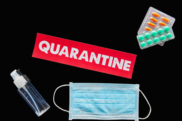 top view of paper with quarantine lettering near pills, medical mask and hand sanitizer isolated on black  - Photo, Image