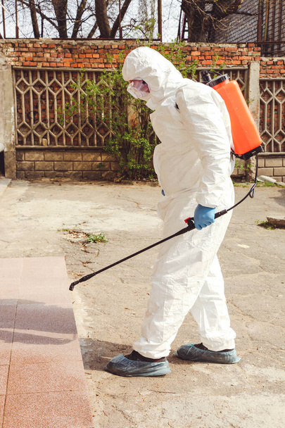 Специалист в защитном костюме с дезинфицирующим распылителем против коронавирусной инфекции на улице. Эпидемический контроль
. - Фото, изображение