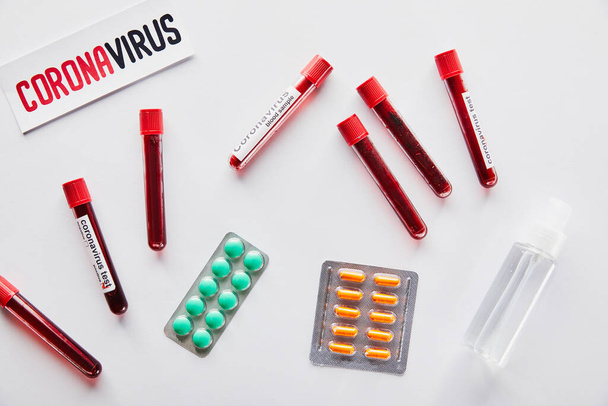 vista superior del papel con letras de coronavirus cerca de tubos de ensayo, desinfectante de manos y pastillas en blanco
  - Foto, Imagen