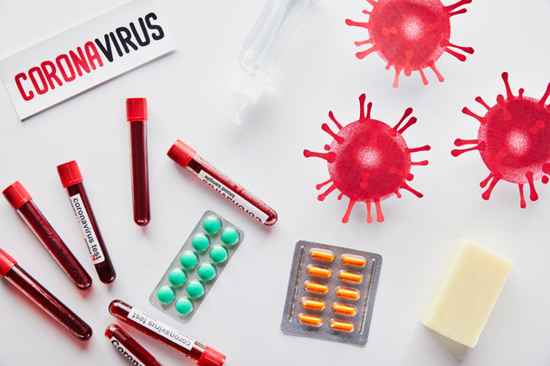 vista dall'alto di carta con scritte coronavirus vicino a virus disegnato, provette, disinfettante per le mani, sapone bar e pillole su bianco
  - Foto, immagini