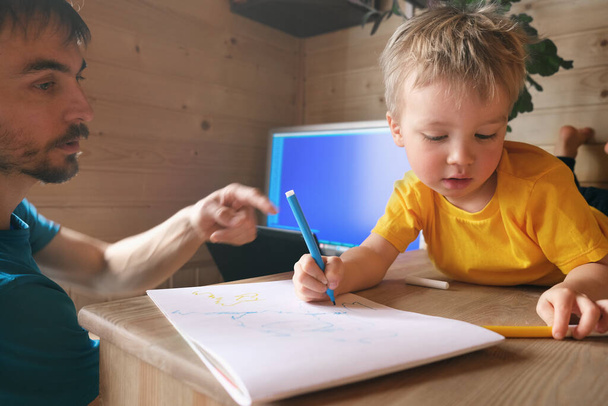 отец фрилансер пытаются работать из дома в карантине и помочь сыну ребенок рисует, концепция родительства многозадачность в самоизолированной образ жизни рабочее место на рабочем месте, домашний офис
 - Фото, изображение