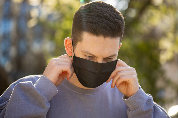 Вирусная маска человека носить защиту лица в профилактике коронавируса. Человек идет по улице с зеленым фоном дерева
 - Фото, изображение