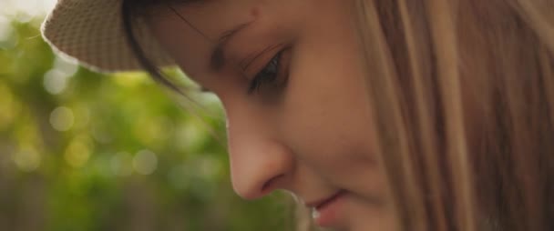 Close up of a beautiful young woman with hat and long brown hair looking down and smiling while working in the garden at sunset. Green bokeh background. SLOW MOTION, SHALLOW DOF, BMPCC 4K.   - Footage, Video
